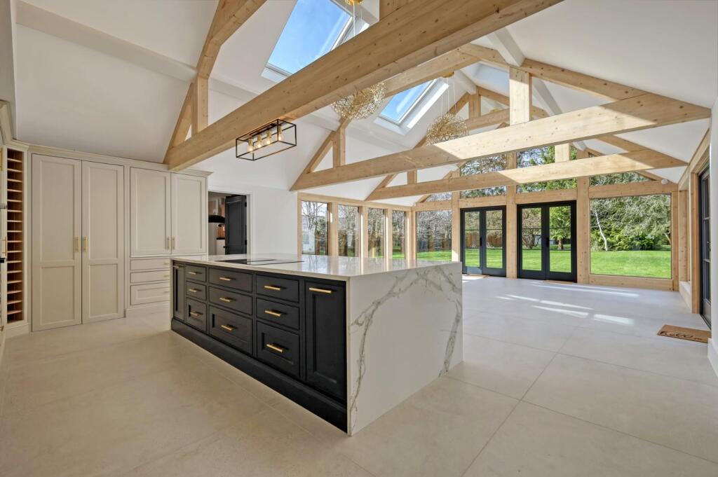 Vaulted open-plan kitchen with painted cabinetry, dark island and exposed timber frame